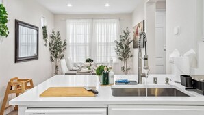 Una cocina moderna con armarios blancos, una isla central con tabla de cortar, un fregadero y un comedor con mesa y sillas.