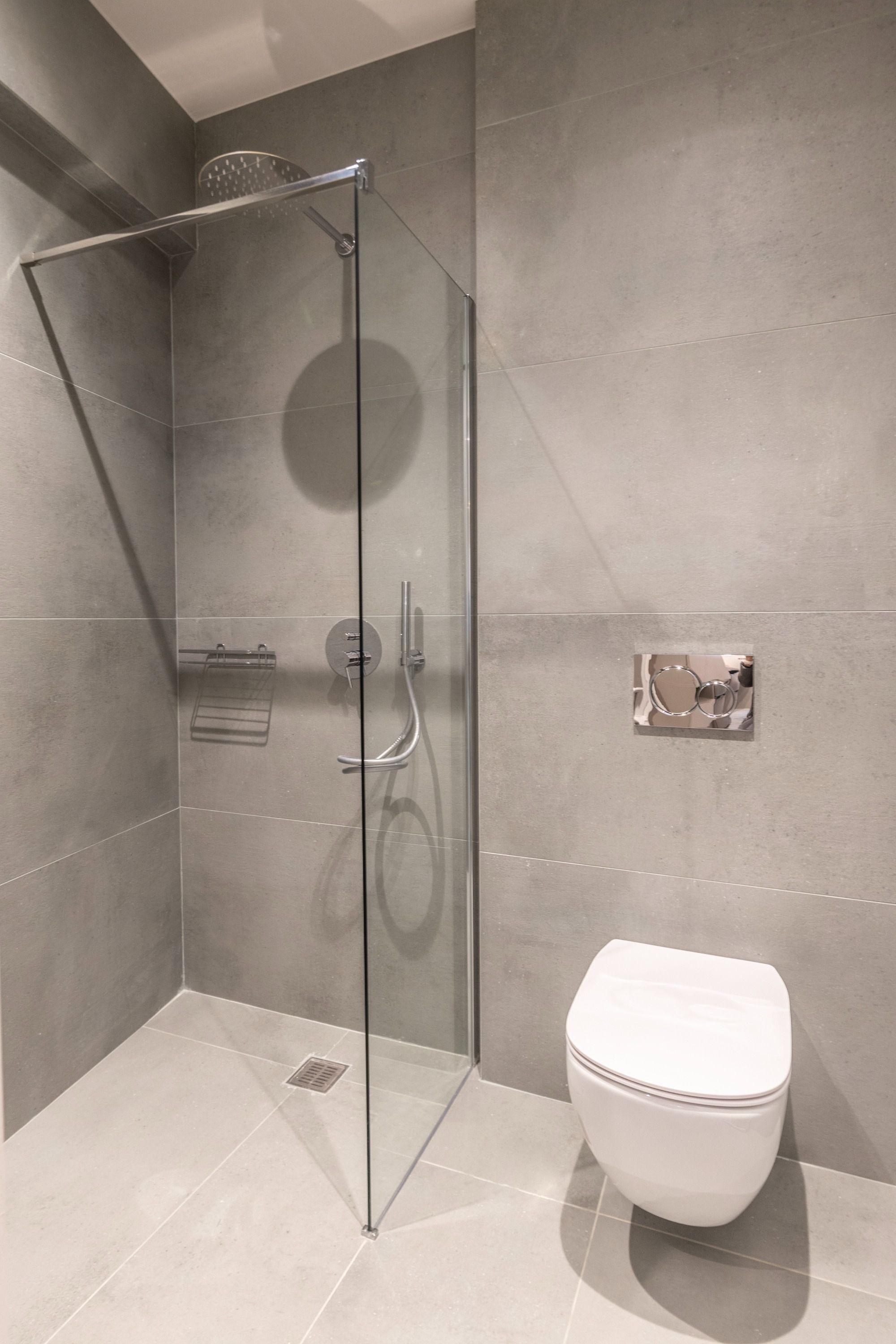Et moderne badeværelse med en brusekabine i glas, et hvidt toilet og en lille hylde med toiletartikler.