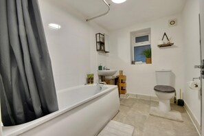 Bathroom features a large bathtub, toilet, and small window.