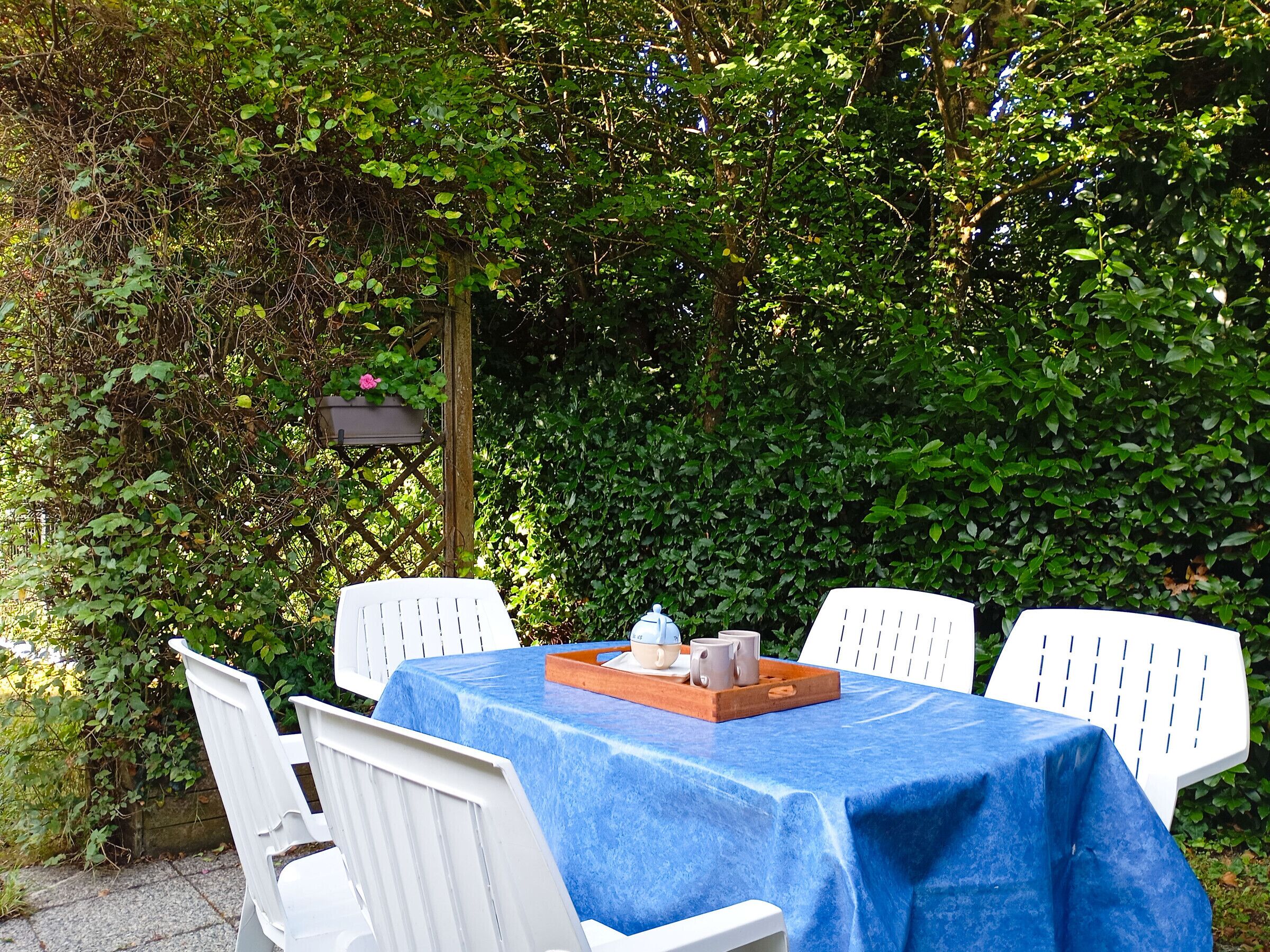 Ein Tisch draußen gedeckt, mit blauer Tischdecke und weißen Stühlen.