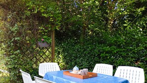 Une table dressée à l’extérieur, recouverte d’une nappe bleue et entourée de chaises blanches.