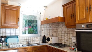 Une cuisine avec des meubles de rangement en bois, une fenêtre ornée d’un rideau en dentelle, une cuisinière et une machine à café.
