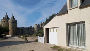 Une cour avec un château en arrière-plan, un bâtiment doté d’une porte blanche et un ciel dégagé.