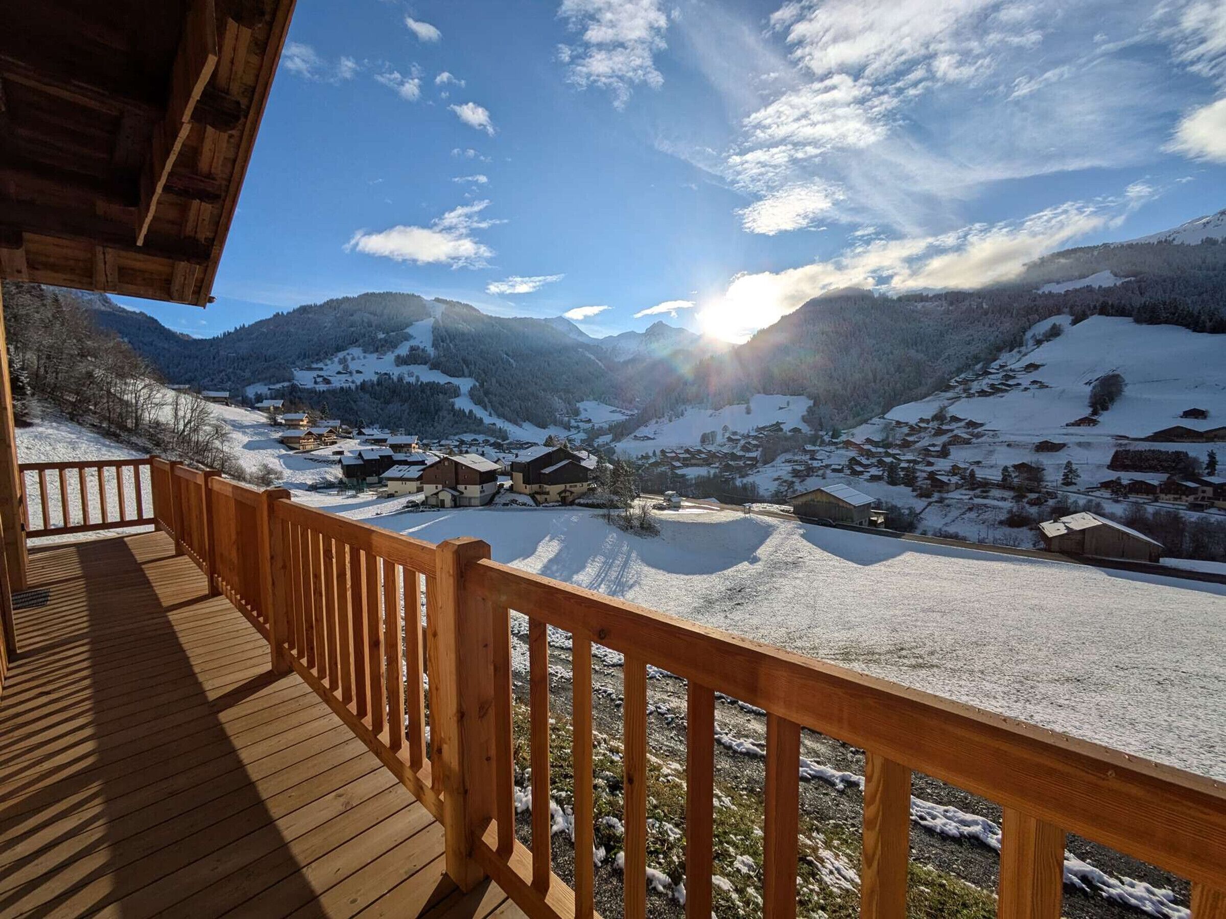 Una terraza de madera con vistas a un pueblo cubierto de nieve y montañas al fondo.