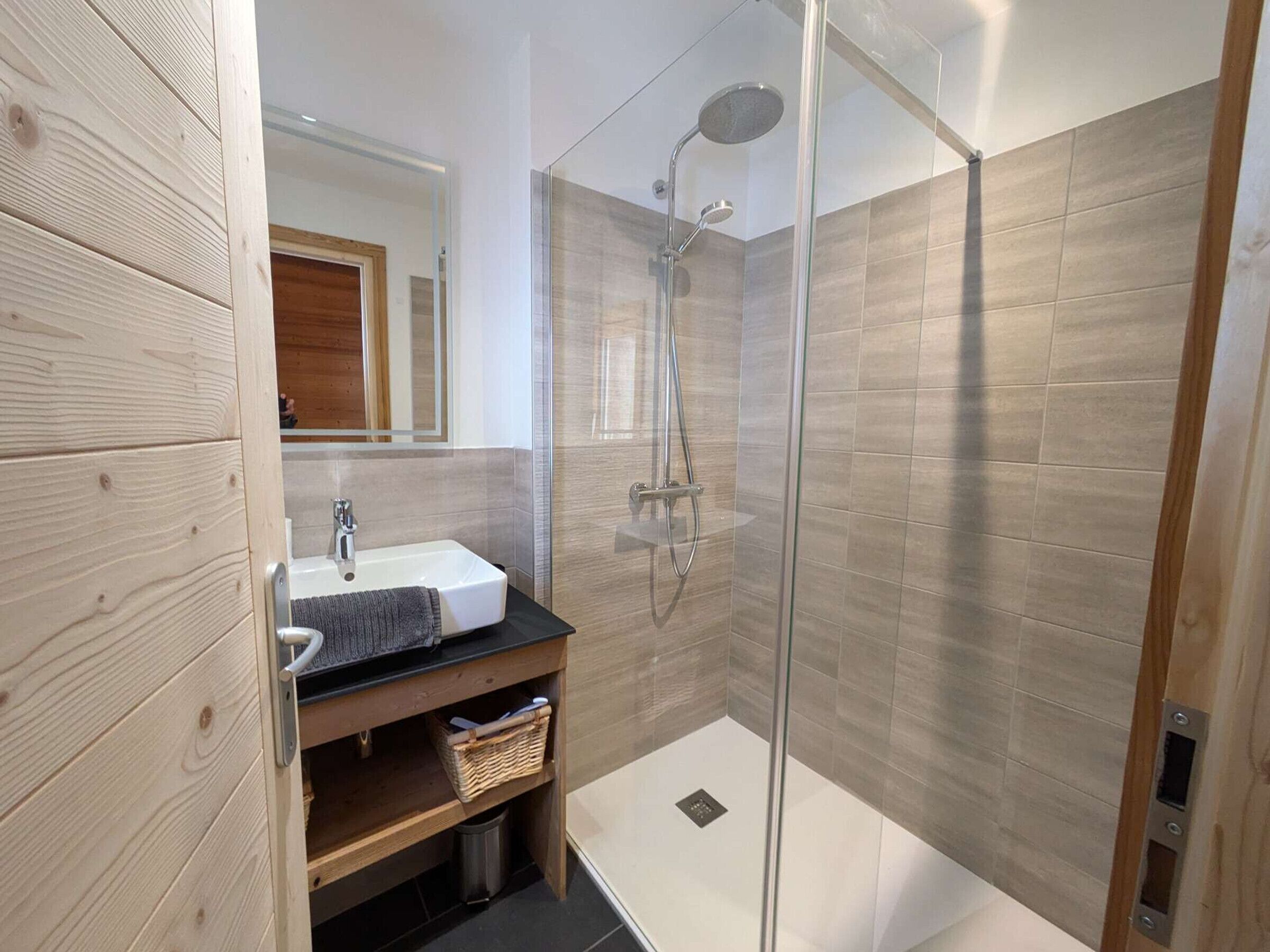 Un baño moderno con ducha de vidrio, tocador de madera y espejo.