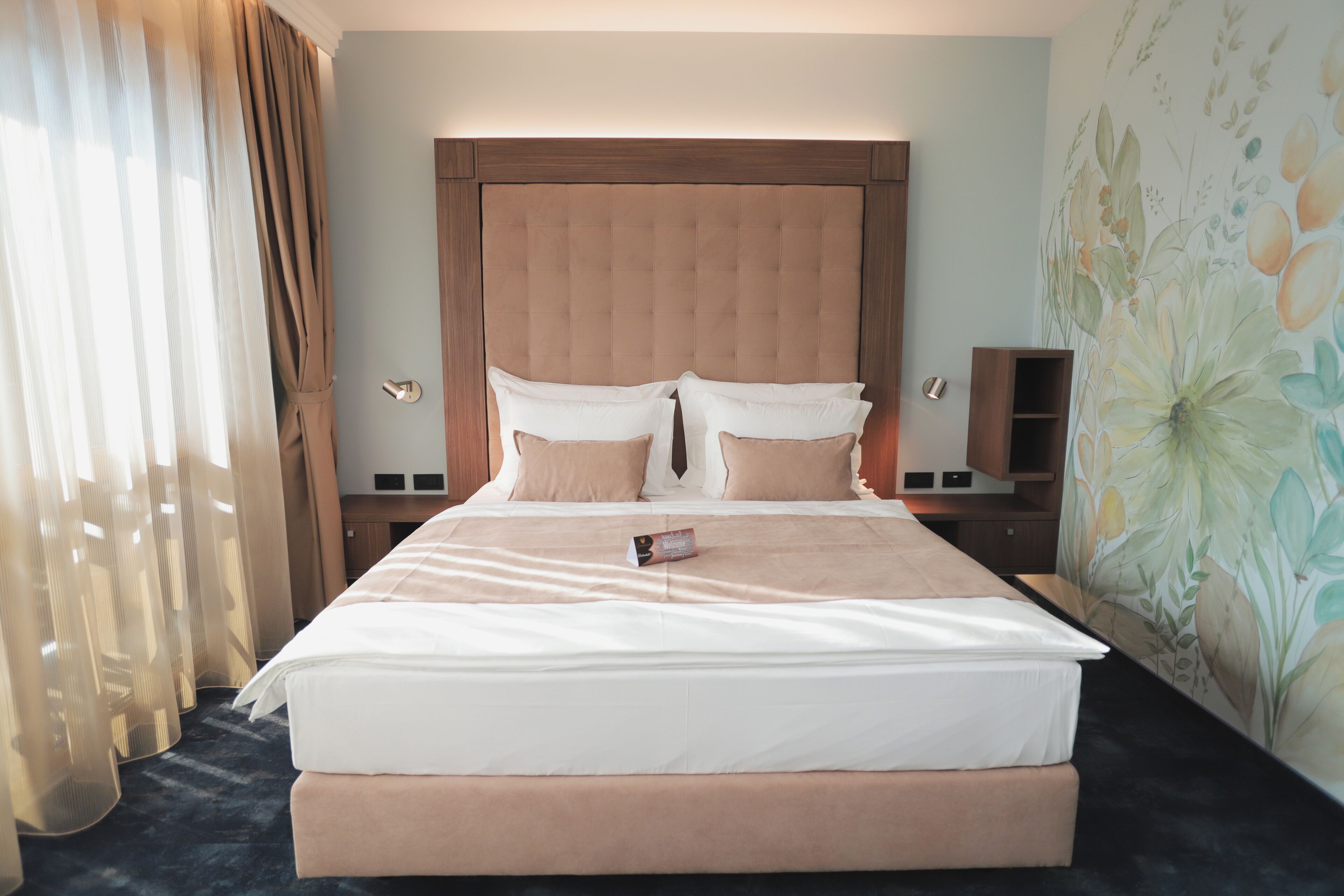 A hotel room with a large bed, a wooden headboard, and a floral wall mural.