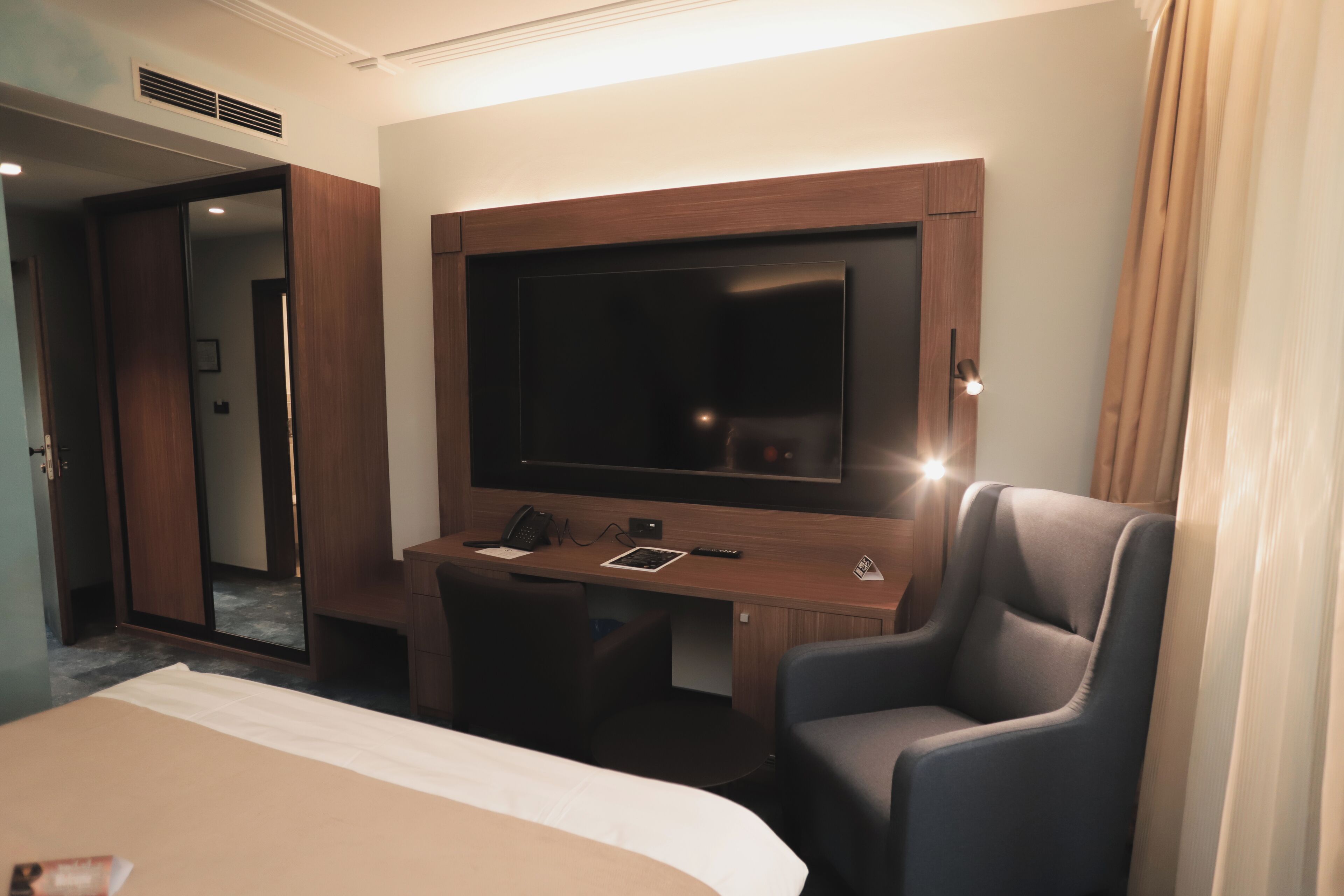 Una habitación de hotel con una cama, un escritorio con televisor de pantalla plana, una silla y una puerta que da a otra habitación.