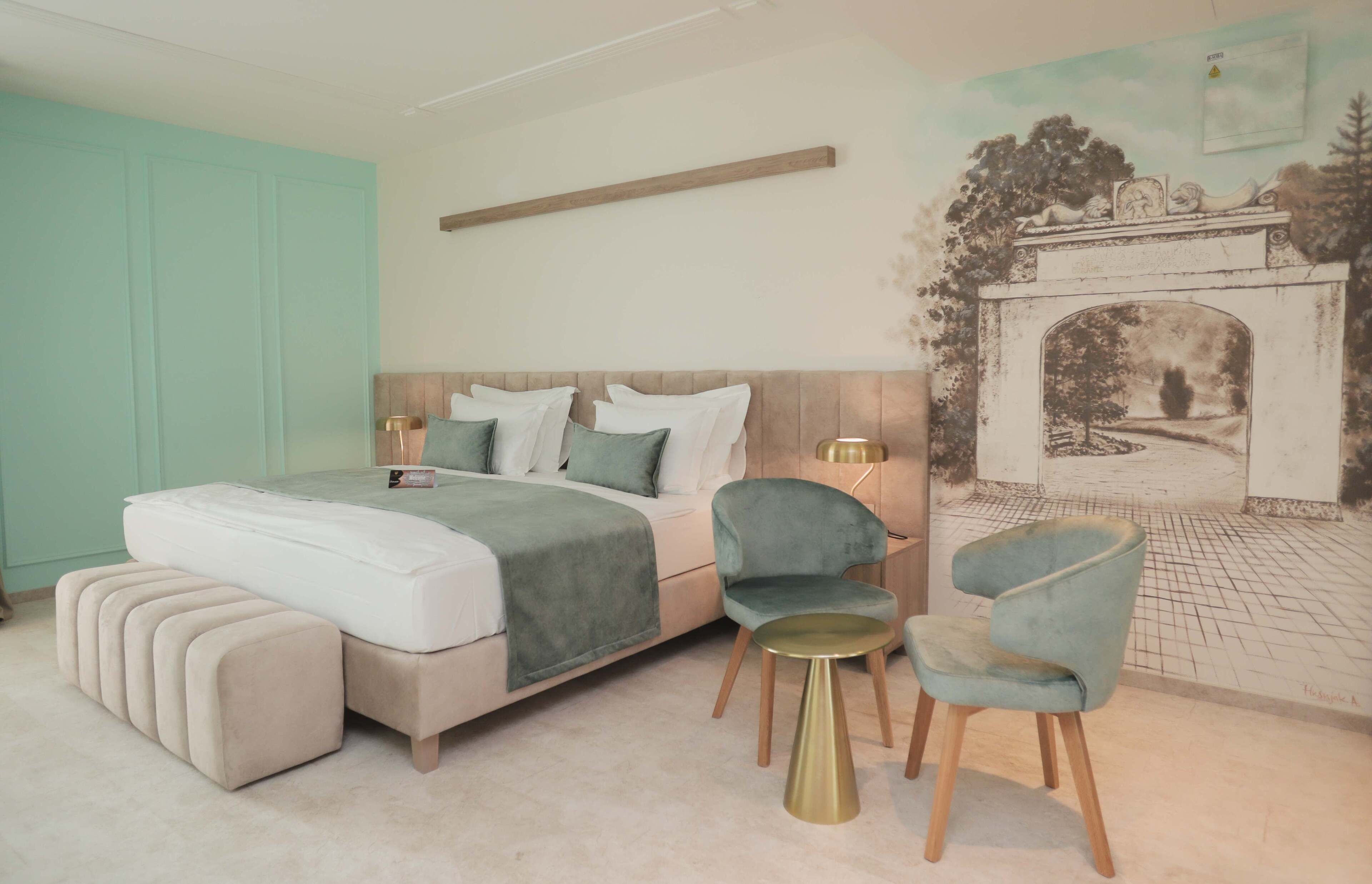 Ein Schlafzimmer mit einem Bett, zwei Stühlen, einem kleinen Tisch und einem Wandgemälde.