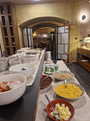 A buffet setup with various food items and containers, including bowls of cereal, yogurt, and other snacks, arranged on a table with a cloth runner.