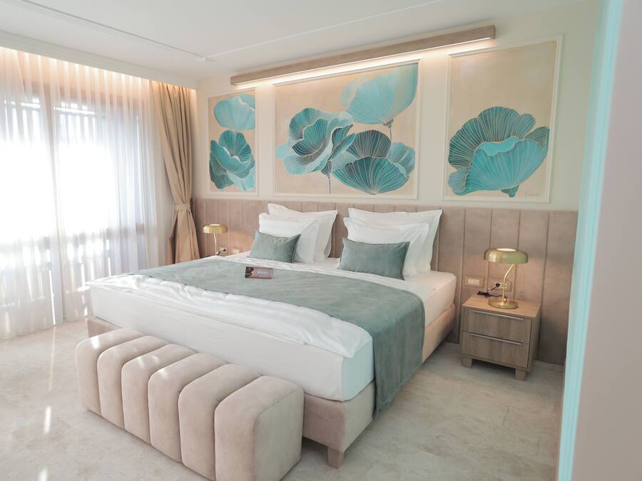 A modern bedroom with a large bed, a bench, two bedside tables, and artwork on the wall.