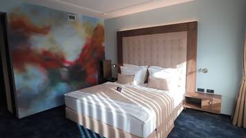 A modern hotel room with a large bed, a headboard, a bedside table, and a wall with abstract art.