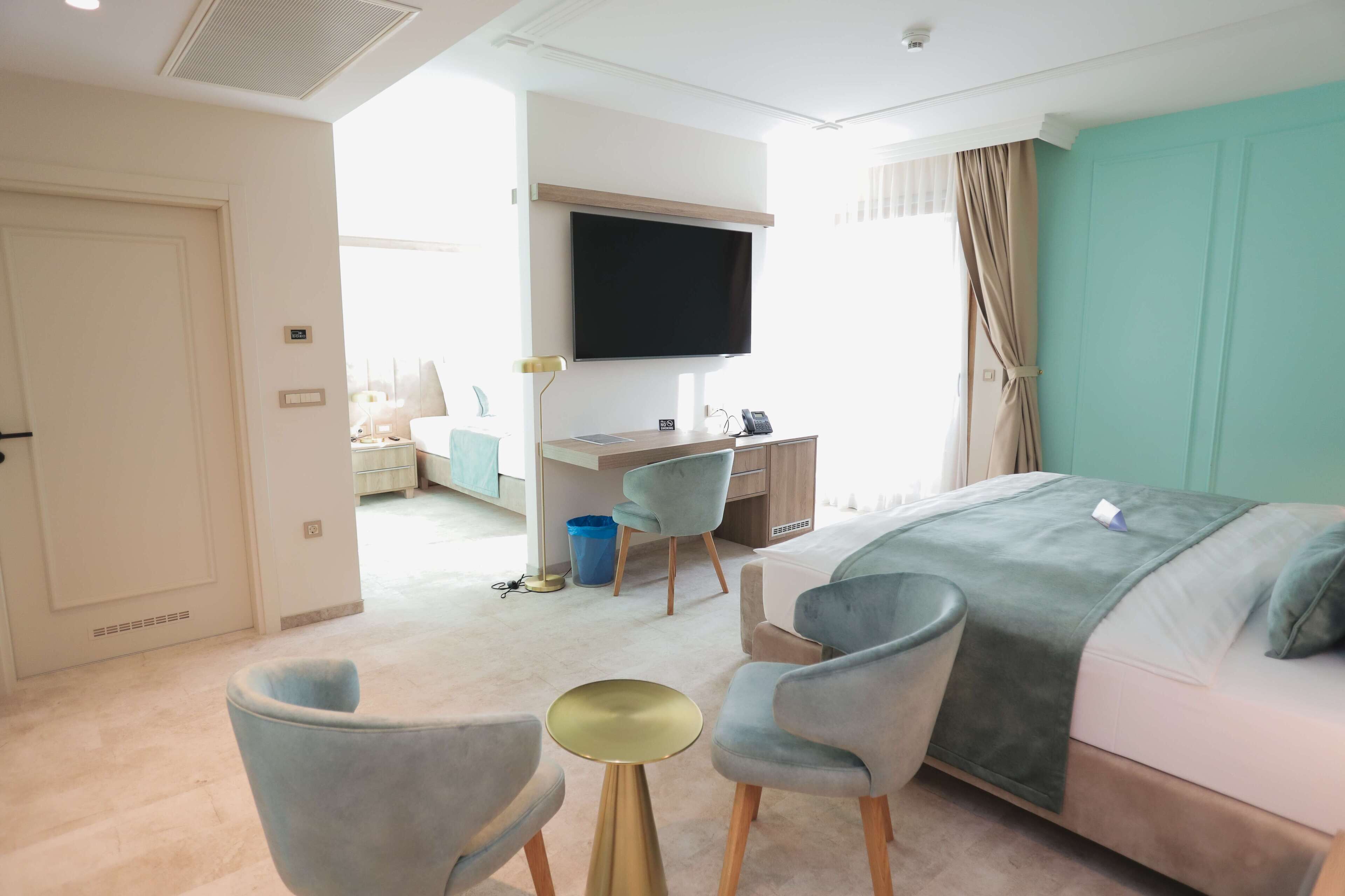 Habitación de hotel con cama, escritorio, silla, televisión y ventana con cortinas.