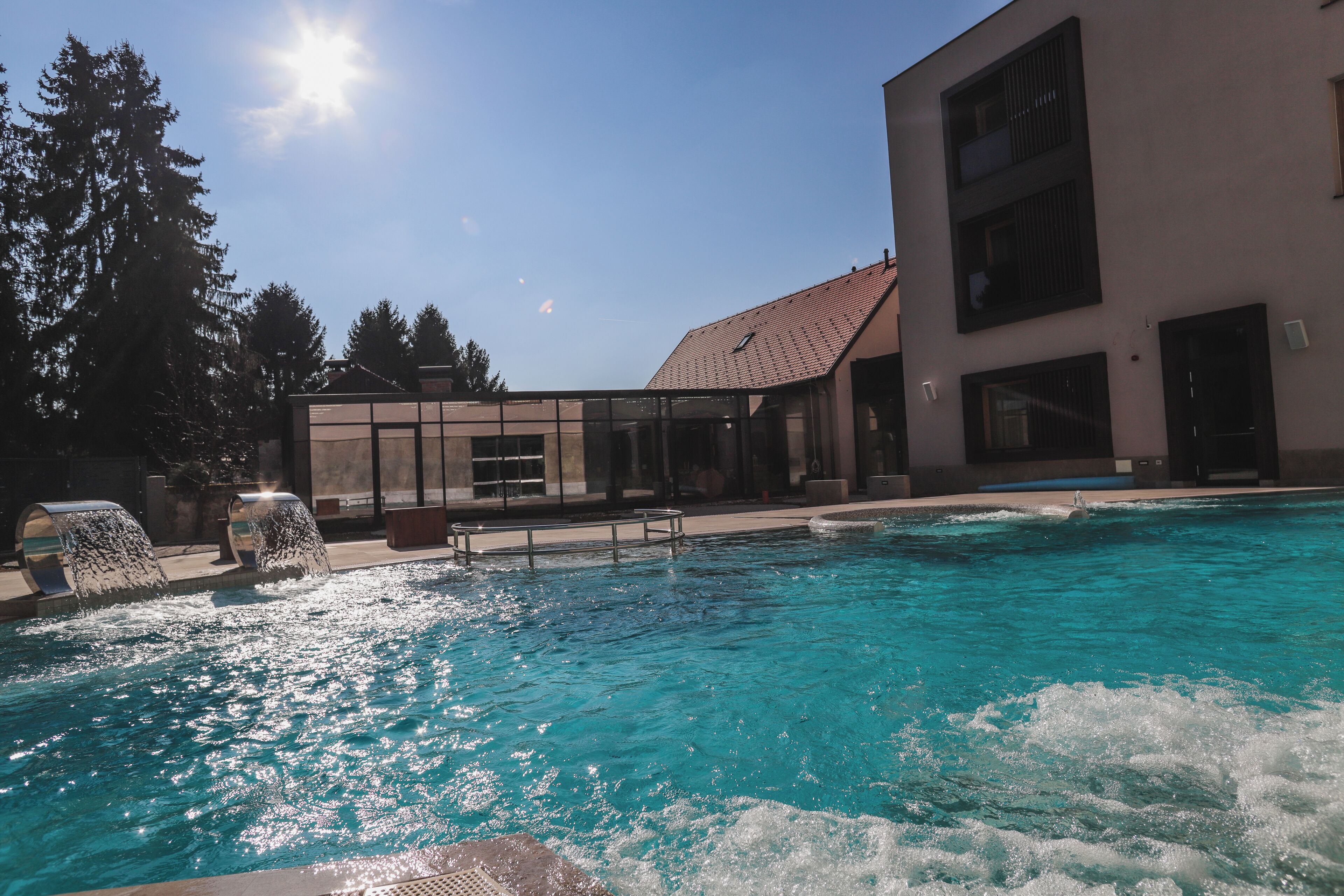 A swimming pool with clear blue water, surrounded by a building with large windows and a tiled roof.
