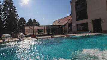 A swimming pool with clear blue water, surrounded by a building with large windows and a tiled roof.