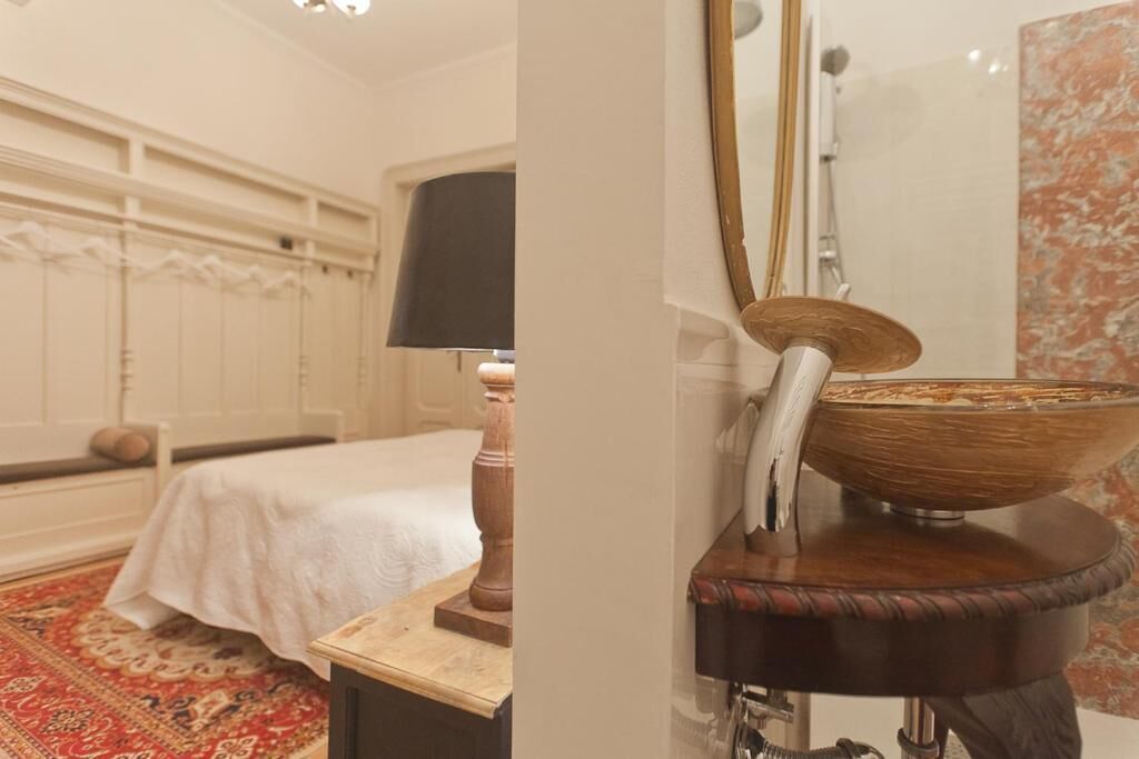 A bedroom with a bed, a nightstand, a lamp, and a large mirror.