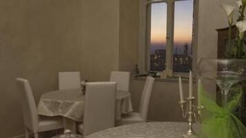 A dining area with a table set for four, a window with a city view, and a vase with flowers.