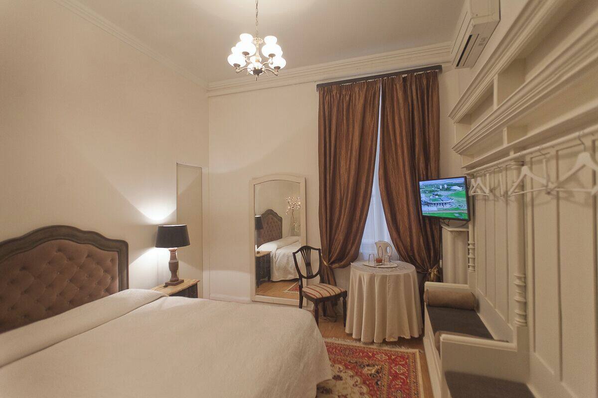 A hotel room with a large bed, a small table with a lamp, a television, and a mirror.