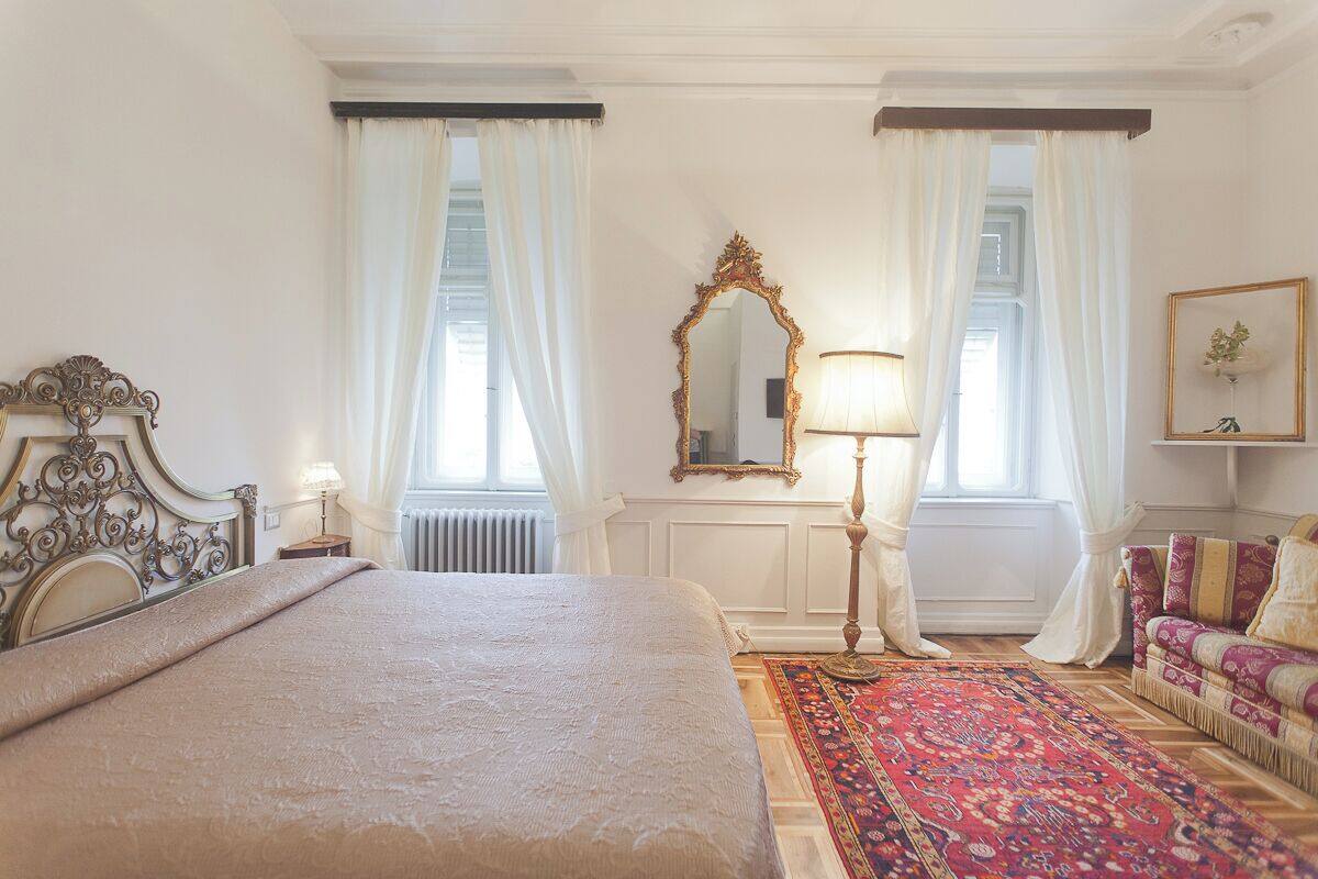 A well-lit bedroom with a large bed, a sitting area with a sofa, a mirror, and a lamp.