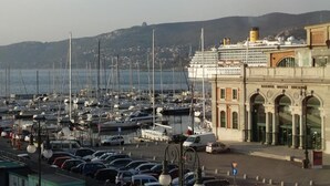 Un port de plaisance où sont amarrés de nombreux bateaux, un grand navire de croisière et un bâtiment historique doté d’entrées en arc de cercle.