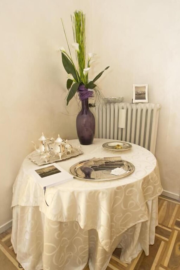 A round dining table with a white tablecloth, a vase with white flowers, and a tray with silverware.