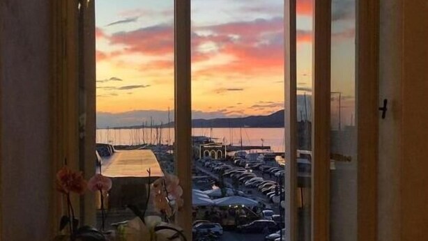 Une pièce dotée d’une grande fenêtre donnant sur une marina où sont amarrés des bateaux.