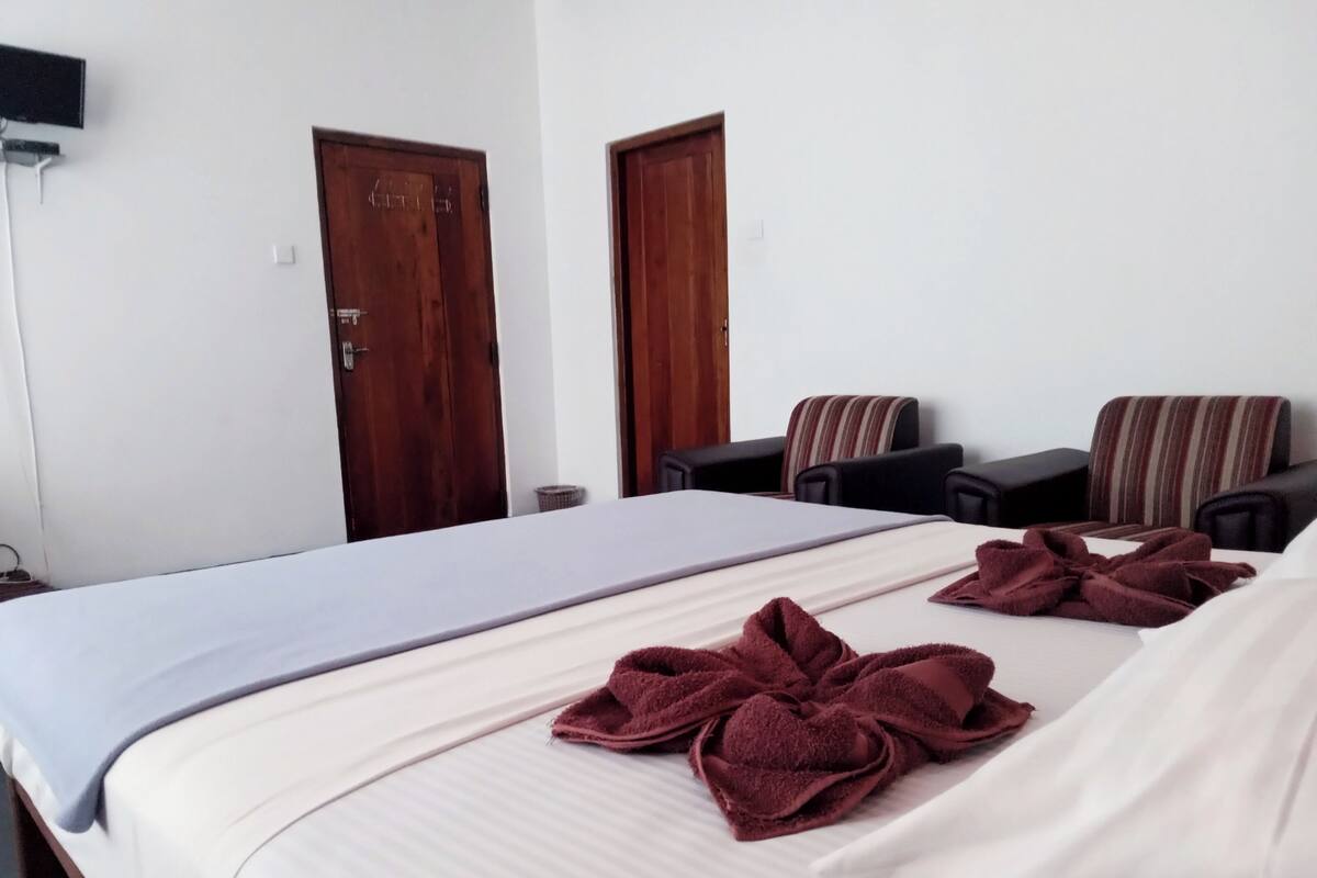 A hotel room with a bed, two wooden doors, a TV mounted on the wall, and two armchairs.
