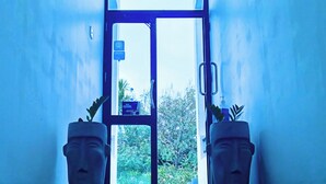 A hallway with a glass door leading to a garden, flanked by two potted plants. - Monarch Ella (Ella)