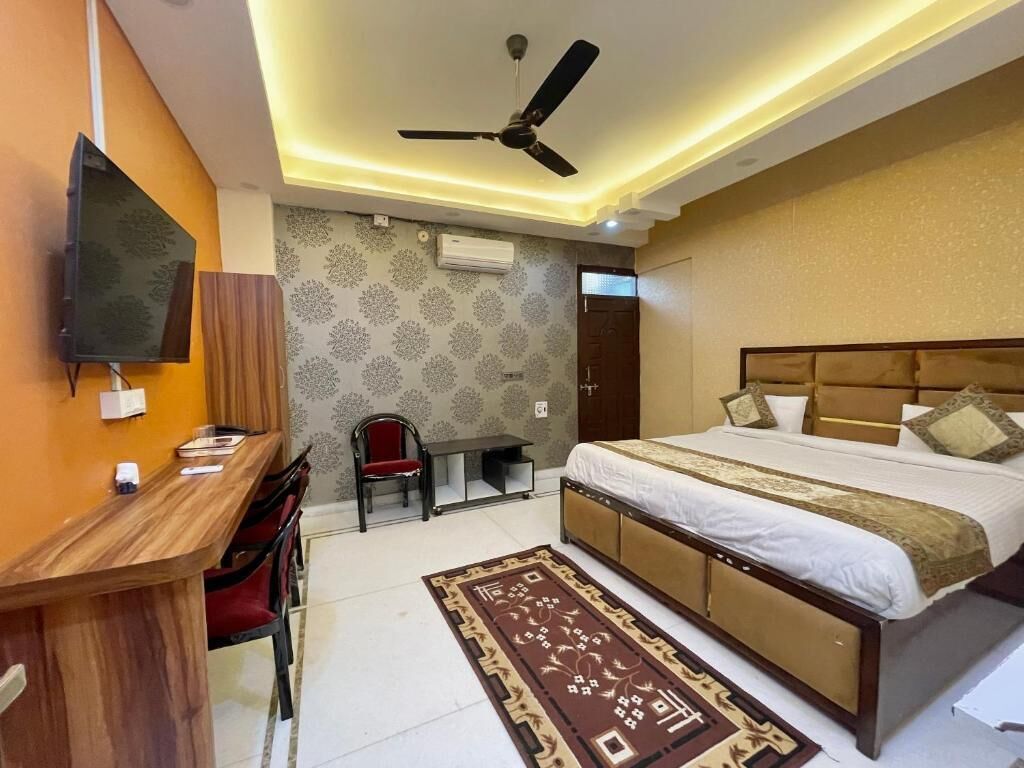 A bedroom with a bed, a desk, a chair, a ceiling fan, and a TV mounted on the wall.