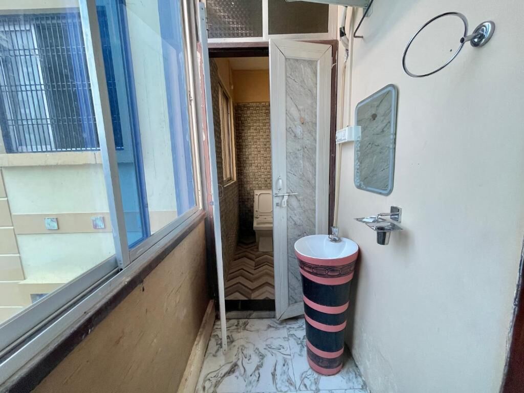 A narrow hallway with a bathroom on the right, featuring a marble floor, a striped sink, and a door leading to another room.
