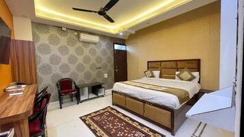 A bedroom with a bed, a desk, a chair, a ceiling fan, and a patterned rug.