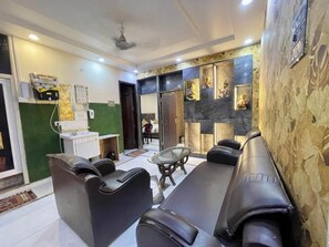 A modern living room with a sofa set, a glass coffee table, and a decorative wall with artwork. - Hotel Shivee - Varanasi (Varanasi)