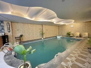 An indoor swimming pool with a modern ceiling design, a clock, and seating areas. - Hotel Shivee - Varanasi (Varanasi)