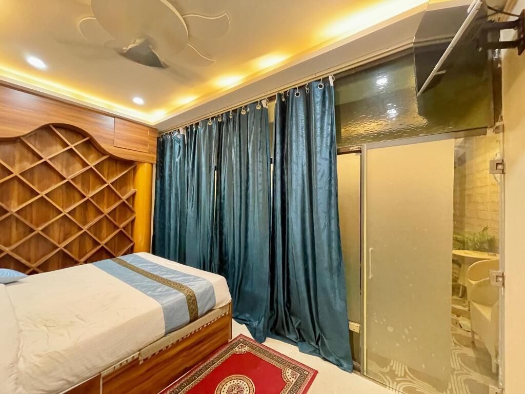 A bedroom with a bed, a wooden headboard, a red patterned rug, and a shower area with a glass door.