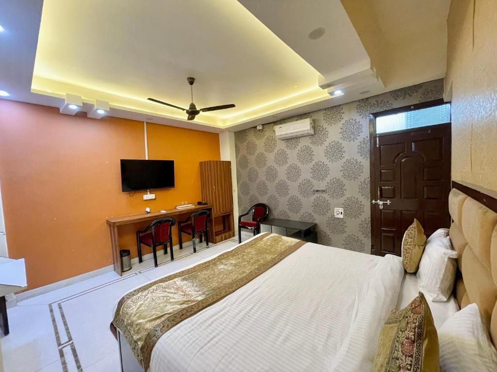 A hotel room with a bed, a desk, a chair, a television, and an air conditioning unit.