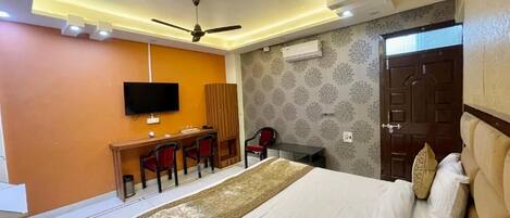 A hotel room with a bed, a desk, a chair, a television, and an air conditioning unit.