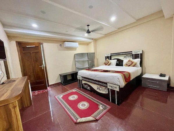 A bedroom with a bed, bedside tables, a desk, and a red patterned rug. - Hotel Shivee - Varanasi (Varanasi)