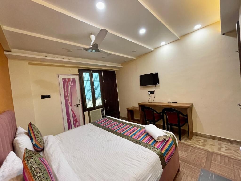 A hotel room with a bed, a desk, a chair, a television, and a ceiling fan.