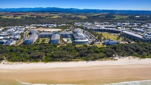 An aerial view of a coastal resort with multiple buildings, a sandy beach, and a clear view of the ocean. - The Pool Resort Kingscliff - 2B Dual Key (7119/20) - Holiday Management Co. (Tweed)