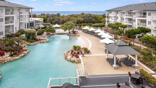 Un resort con piscina, sillas de descanso y vista al océano.