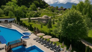 A swimming pool with lounge chairs and umbrellas, surrounded by greenery and a mountain in the background. - Regnum Banya Thermal Hotel (Razlog)