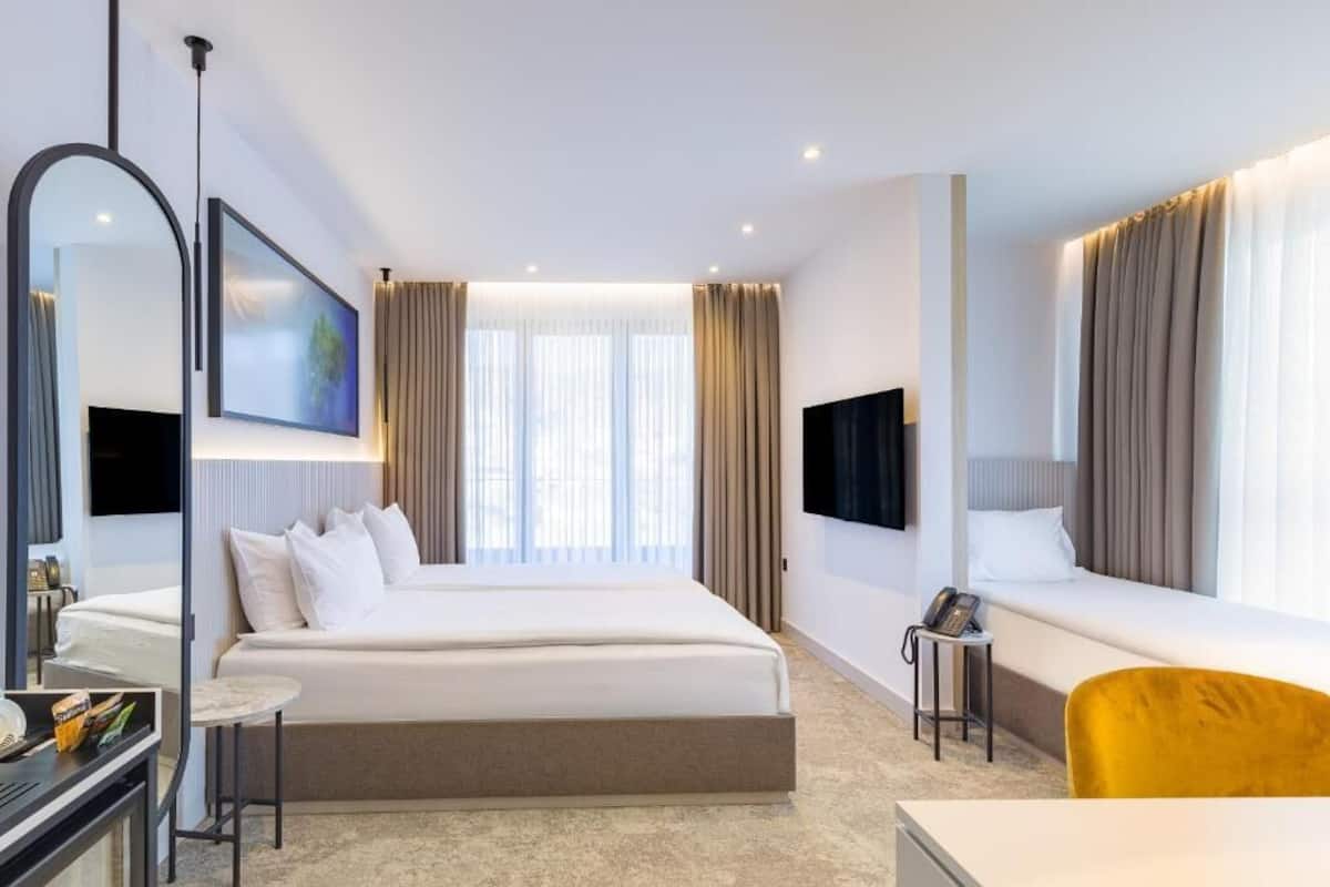 A modern hotel room with a large bed, a bedside table, a chair, a desk, a mirror, and a TV.