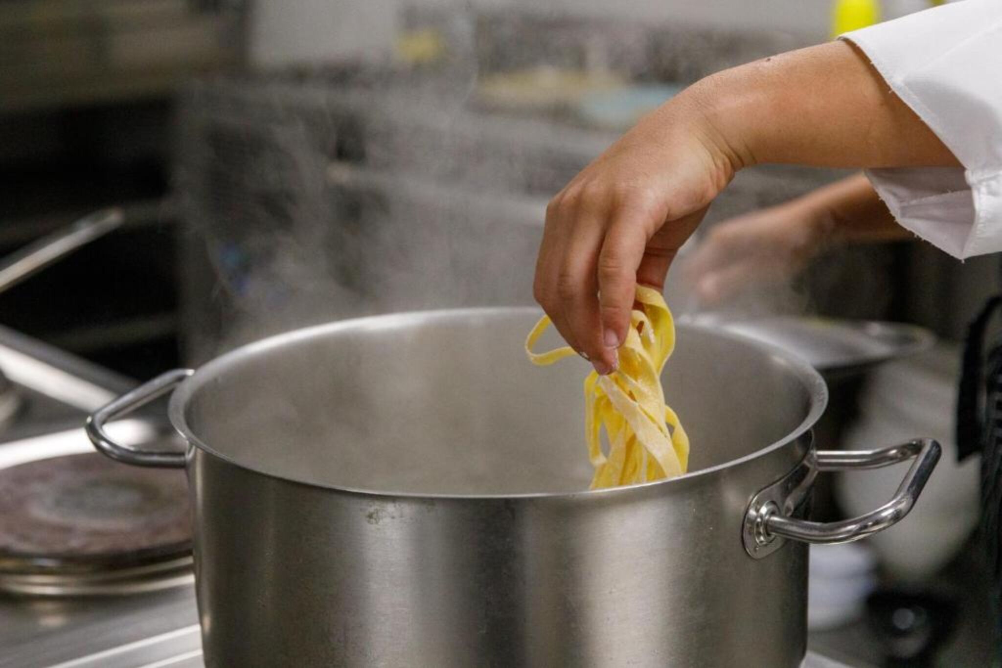 A hand holding a piece of pasta over a stainless steel pot.
