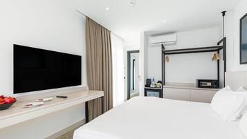 A modern hotel room with a large bed, a flat-screen TV mounted on a wall, a desk with a chair, and a bunk bed.