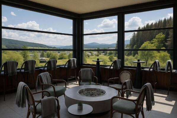 A room with a circular seating area around a central fire feature, large windows offering a view of a green landscape with trees and hills. - Regnum Banya Thermal Hotel (Razlog)