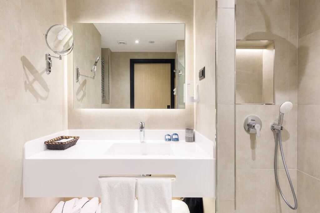 A modern bathroom with a white sink, a mirror, a towel rack, and a shower area.