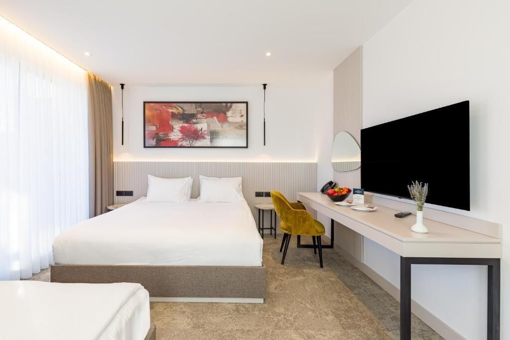 Ein modernes Hotelzimmer mit einem großen Bett, einem Schreibtisch mit Stuhl, einem Flachbildfernseher und einem Bild an der Wand.