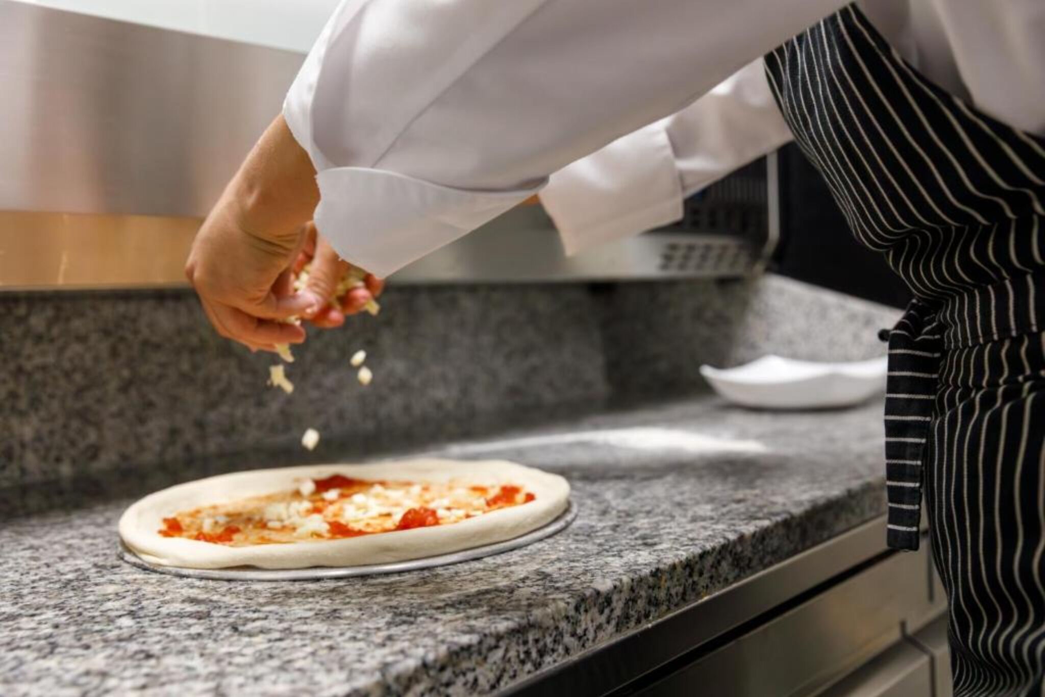 Henkilö valmistaa pizzaa keittiön työtasolla.