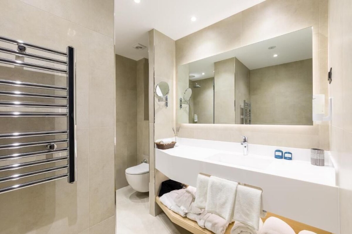 A modern bathroom with a large mirror, a white sink, and a towel rack.