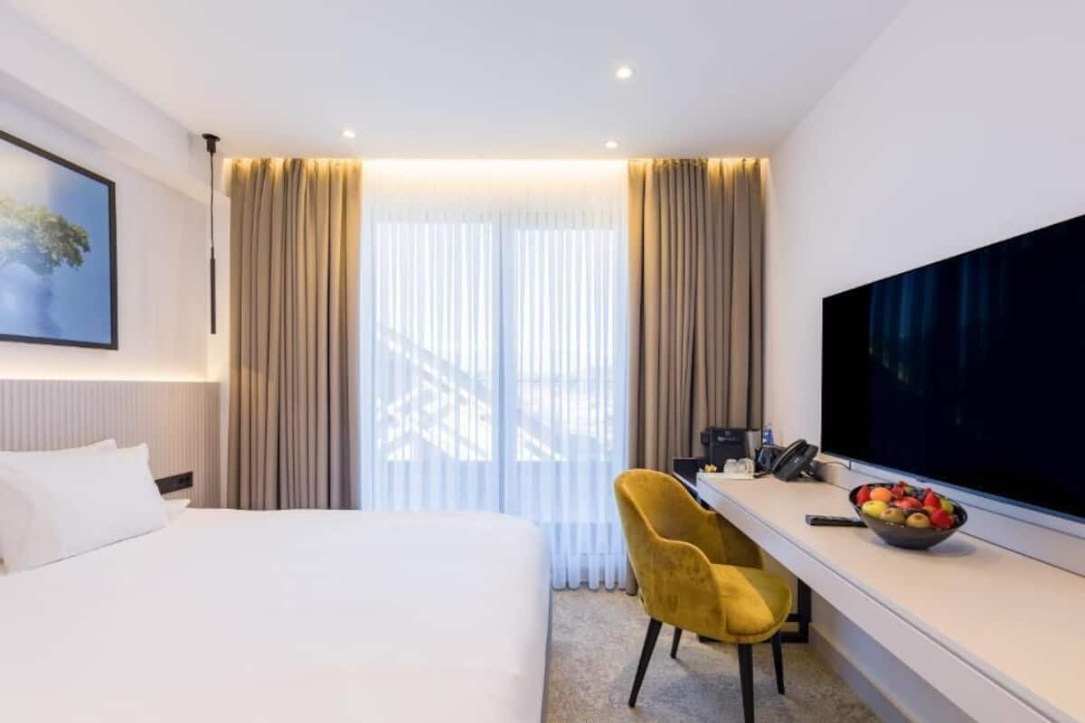 A hotel room with a bed, a desk with a computer, a TV, and a fruit bowl.