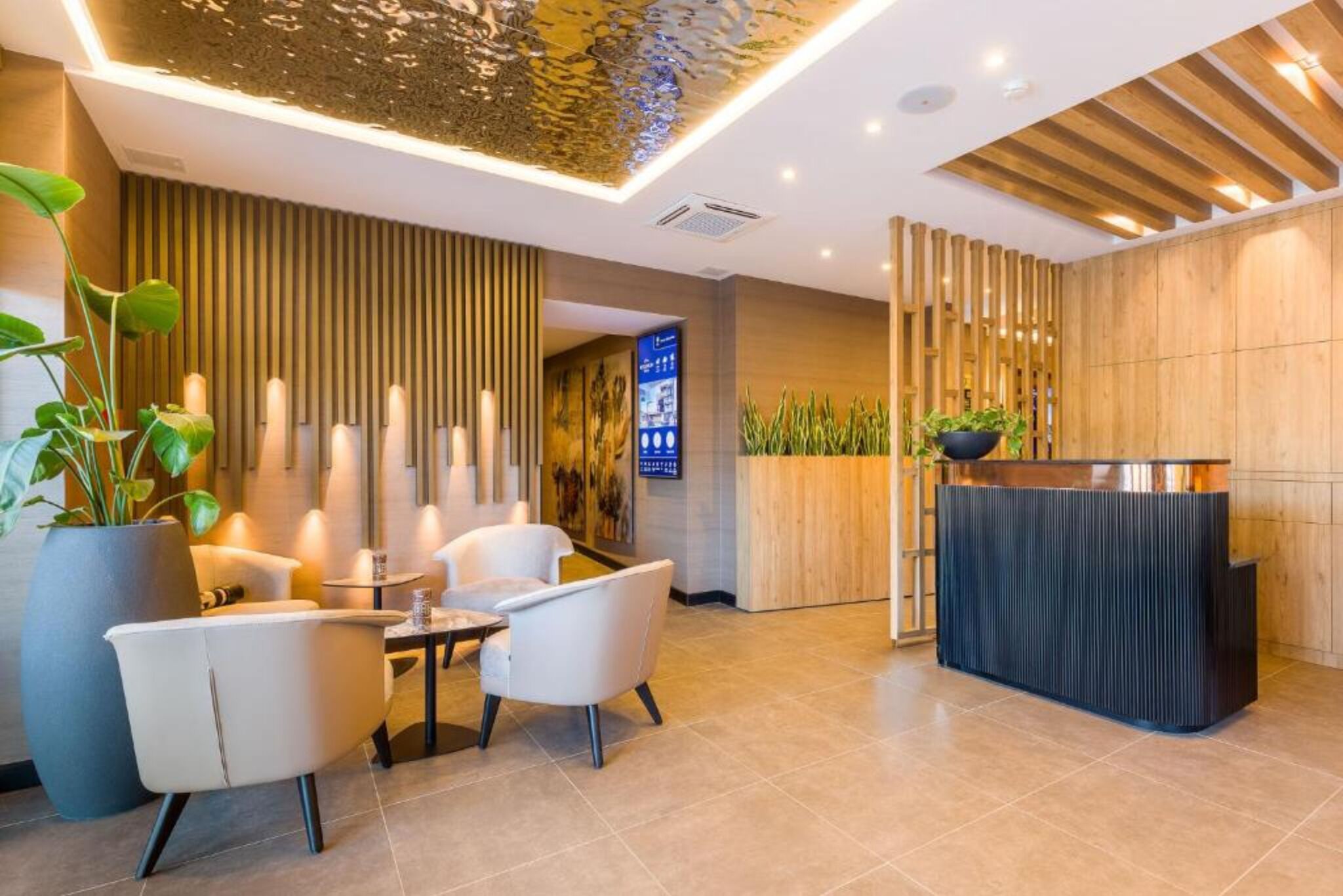 A modern reception area with a wooden reception desk, a seating area with two chairs and a small table, and a large potted plant.